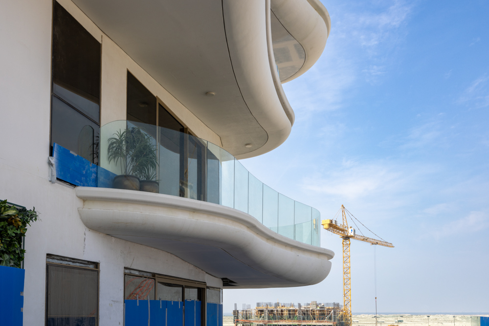 Beach Walk Residence A modern building with a curved balcony, featuring glass railings and a construction crane in the background.